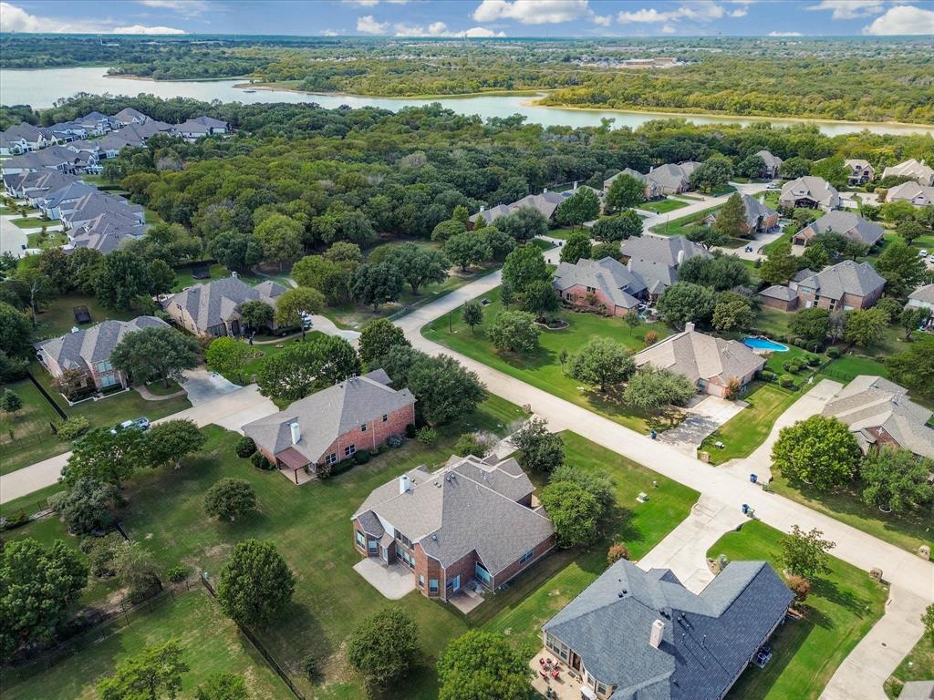 Aerial perspective of residential community featuring brick-and-stone exteriors, composition shingle roofing, expansive green lots, and mature tree canopy with proximity to water