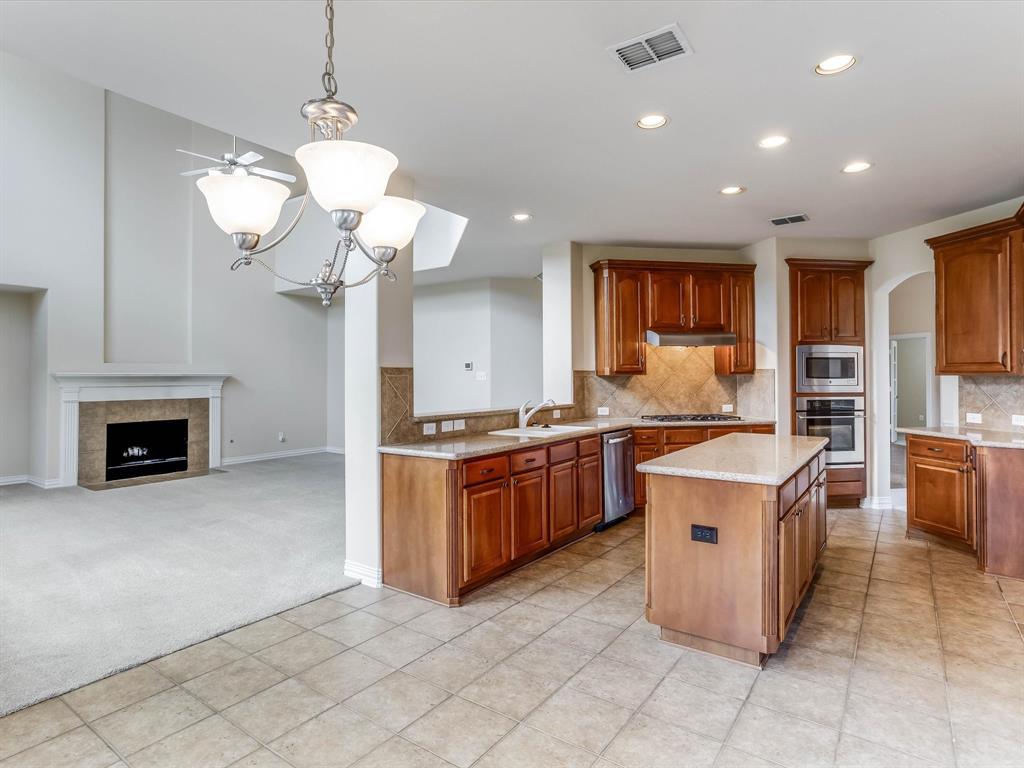 Kitchen featuring wood cabinetry, stone-finish countertops, tile backsplash, built-in wall oven, and a center island, complemented by a fireplace with stone surround