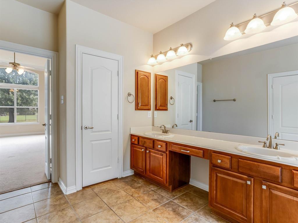 Double vanity featuring wood cabinetry, stone countertops, dual integrated sinks, oversized wall-to-wall mirror, and ceramic tile flooring