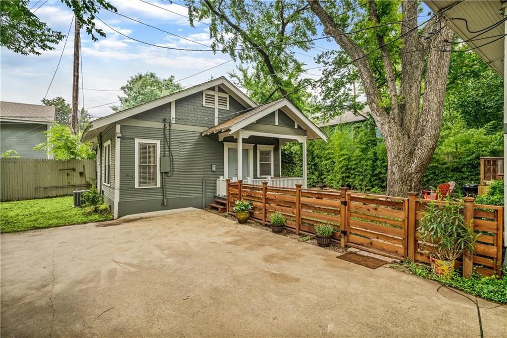 Exterior featuring horizontal lap siding, a gabled roofline, a covered front porch, a concrete parking area, and a horizontal wood-slat fence
