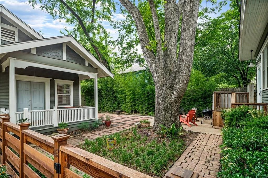 Covered front porch with white railing, brick-paved patio, mature shade tree, and wood-slat privacy fencing