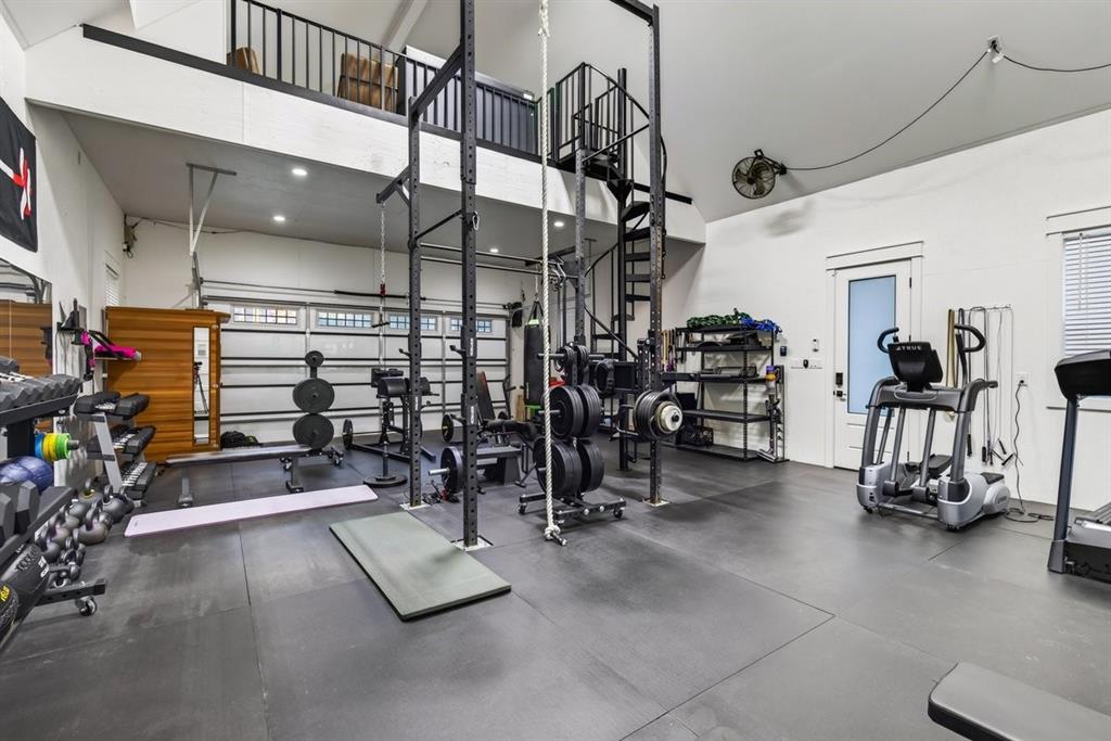 Oversized garage converted into a fully equipped home gym with high ceilings, rubber flooring, and an upstairs loft.