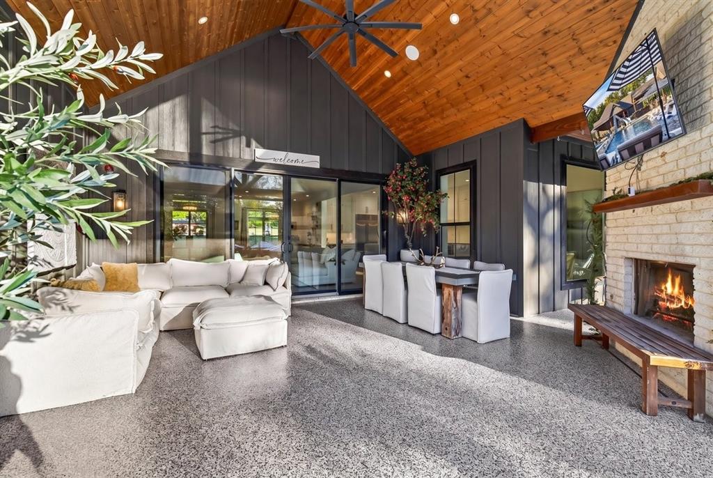 Covered outdoor living area with exposed wood ceiling, wood-burning fireplace, and motorized MagaTrac screens and multiple seating areas.