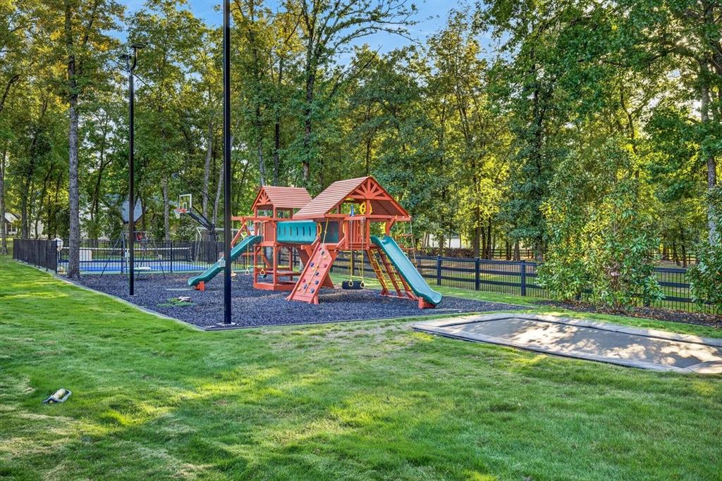 Expansive backyard featuring a playground, trampoline, and basketball court surrounded by mature trees.