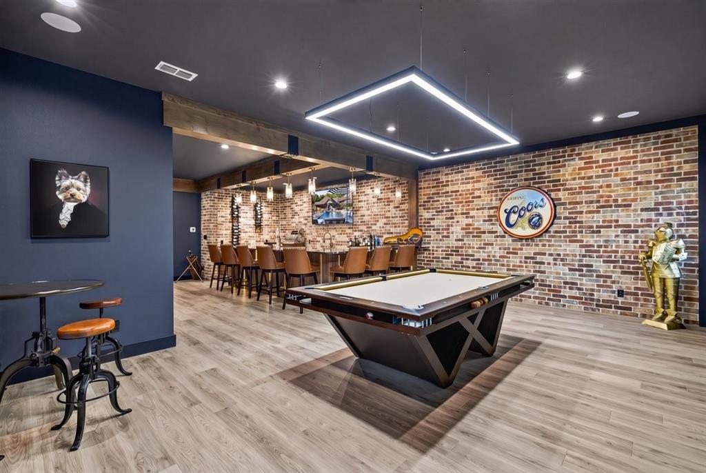 Expansive game room featuring a pool table, custom lighting, and a full bar with seating for guests.