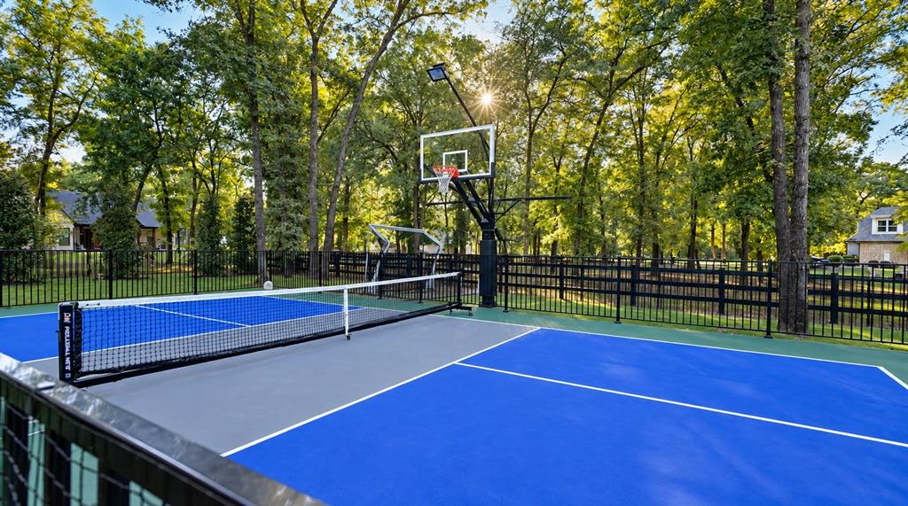 Fenced pickle ball court with basketball hoop with overhead light.