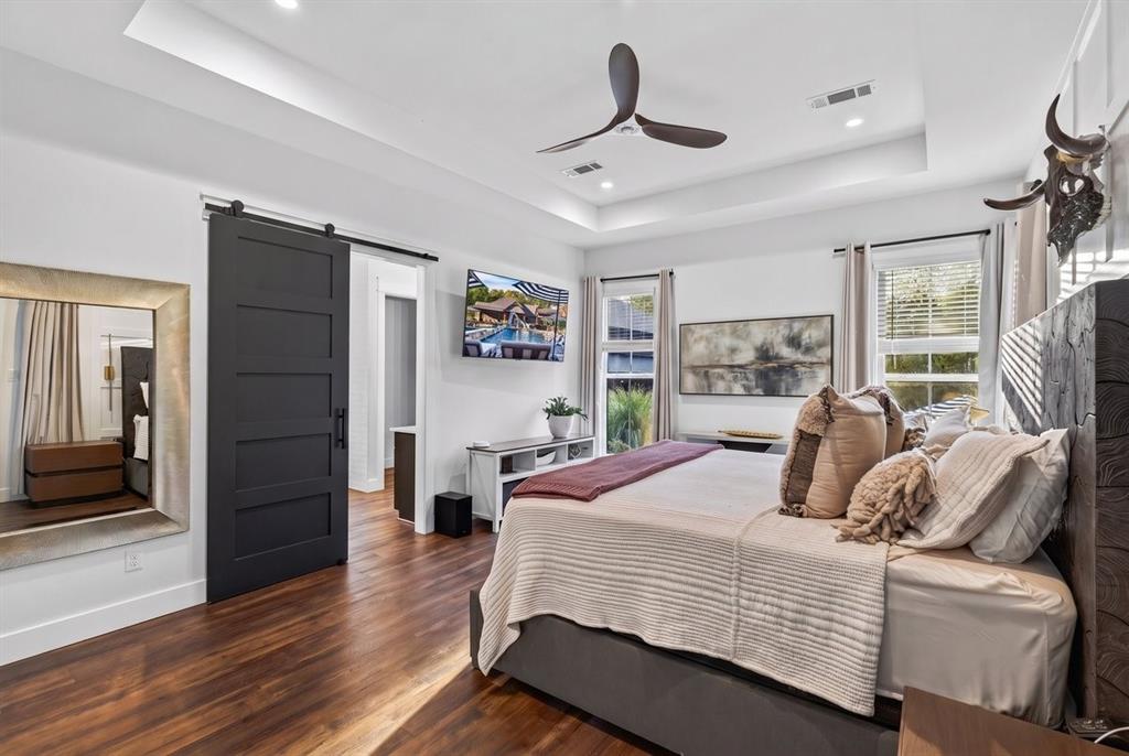 Primary bedroom with tray ceiling, modern ceiling fan, large windows, and a door directly out to the patio! Main Residence.