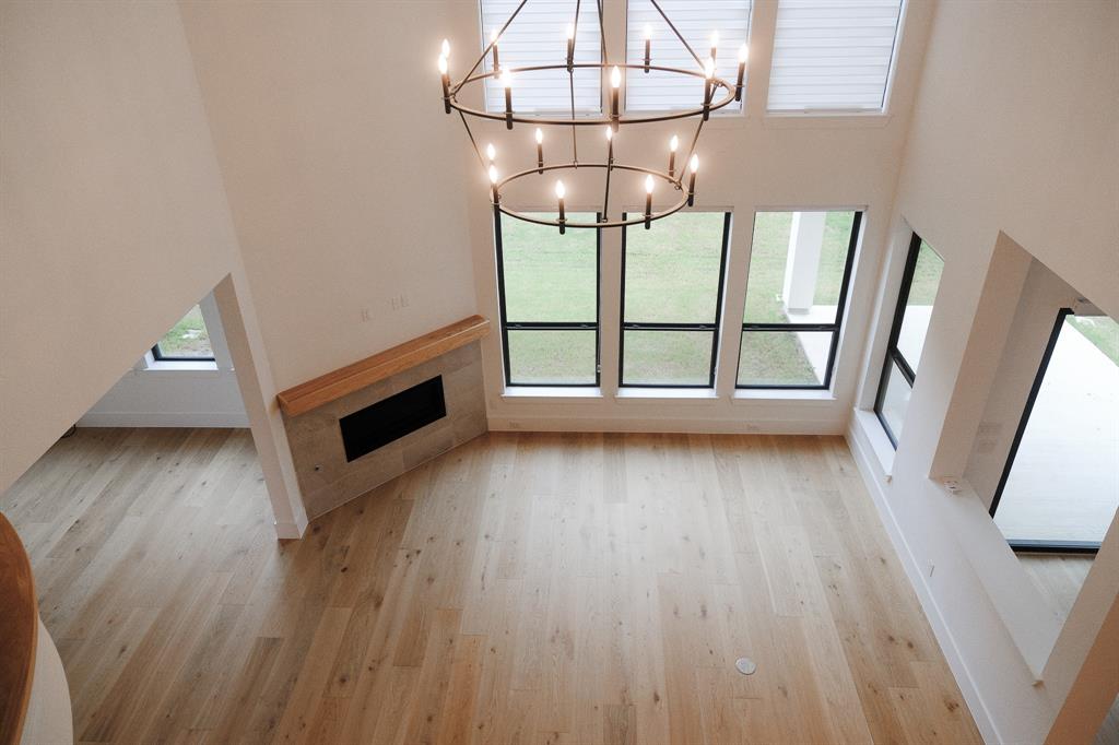 Double-height living area featuring wood-finish flooring, a contemporary iron chandelier, a floor-to-ceiling window arrangement, and a fireplace with a light-tone tile surround and wood mantel