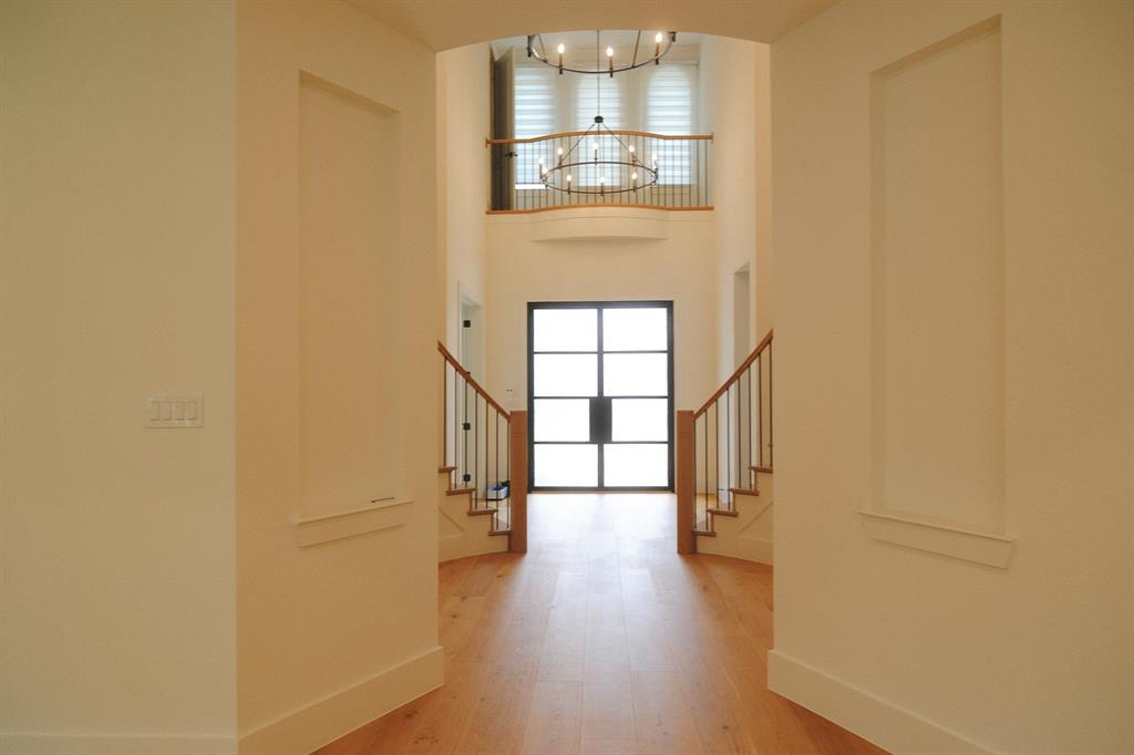 Foyer featuring wood-finish flooring, two recessed wall niches, dual-staircase architecture with wooden handrails, and a multi-panel grid-style door