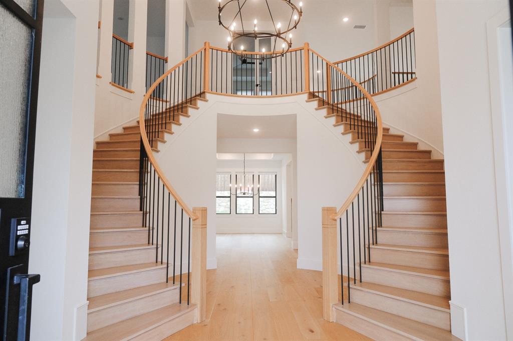Grand dual-staircase foyer featuring wood-finish treads, metal balusters, polished wood handrails, and a large multi-tiered iron chandelier