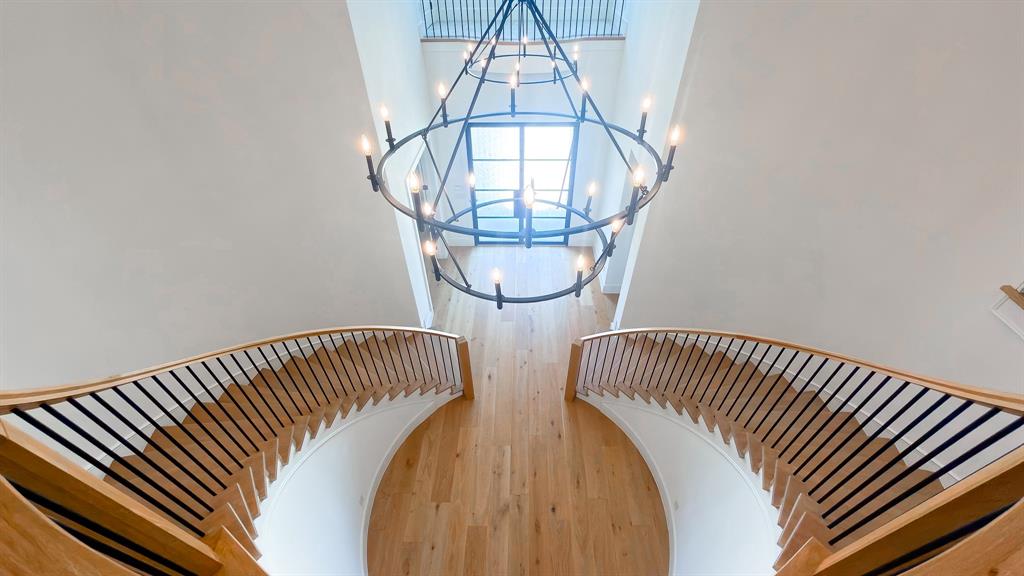 Double curved staircase with wood treads and handrails featuring thin black metal balusters, large metal multi-tier chandelier, and wood-finish flooring