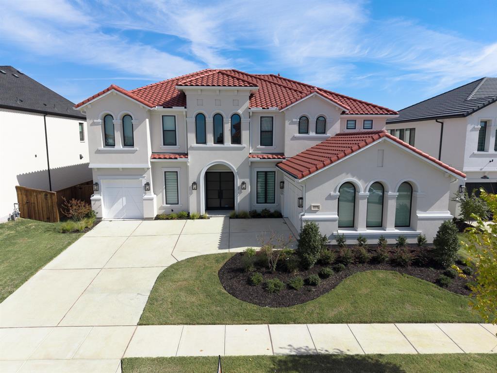Mediterranean-inspired exterior featuring a clay tile roof, stucco facade, arched entryway, multi-paned arched windows, and a paved multi-car driveway Mediterranean-inspired exterior featuring a clay tile roof, stucco facade, arched entryway, multi-paned arched windows, and a paved multi-car driveway