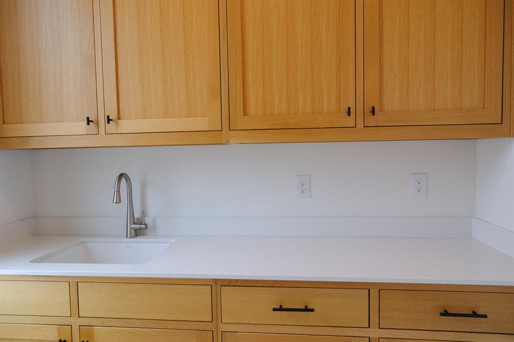 Laundry Room Sink, Light-toned wood cabinetry, clean-lined white stone countertops, an integrated white undermount sink, a sleek stainless steel gooseneck faucet, and matte black hardware