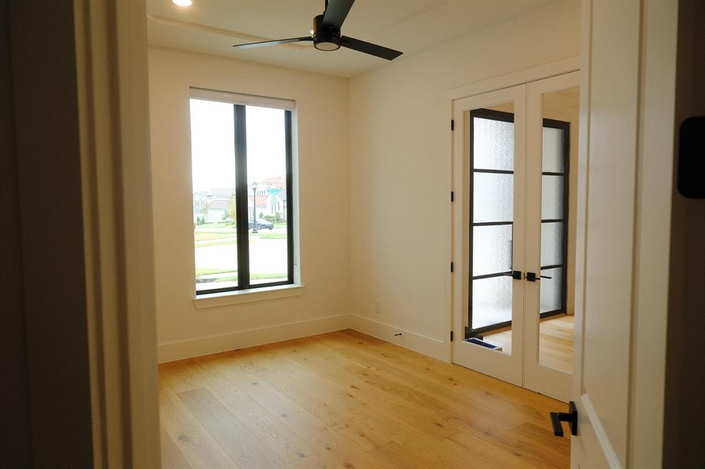 Study Room featuring wood-finish flooring, a matte black ceiling fan, a vertical window with black trim, and French doors with mullioned glass panes