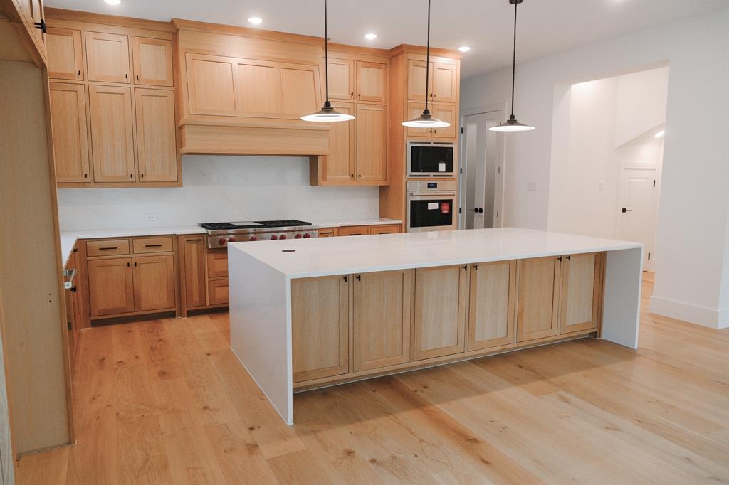 Kitchen featuring natural wood cabinetry, waterfall-edge island, wood-finish flooring, built-in double wall ovens, and three pendant lights