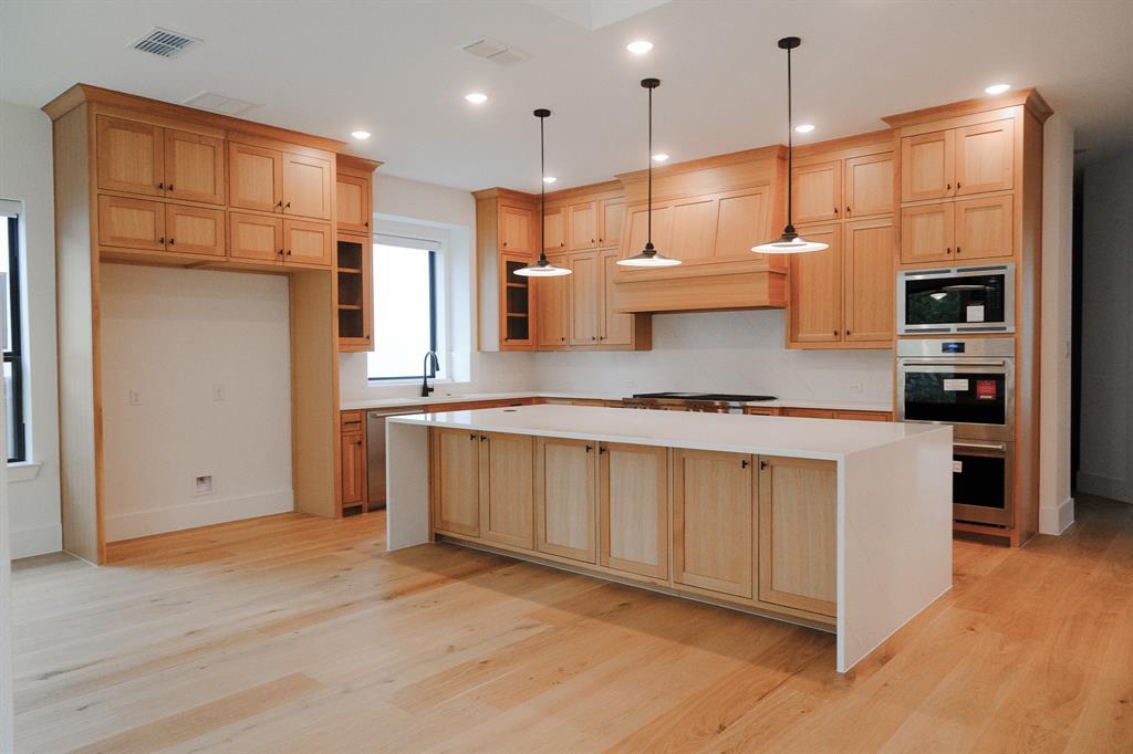 Kitchen featuring light wood cabinetry, a central island with a waterfall countertop, integrated stainless steel appliances, and pendant lighting