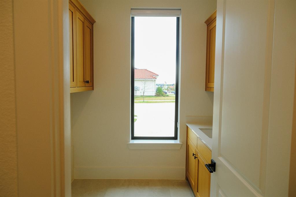 Laundry Room vertical window, wood-finish cabinetry, stone countertop with integrated sink, and matte black hardware