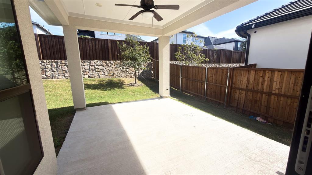 Covered concrete patio featuring a ceiling fan, privacy wood fencing, and stone retaining wall