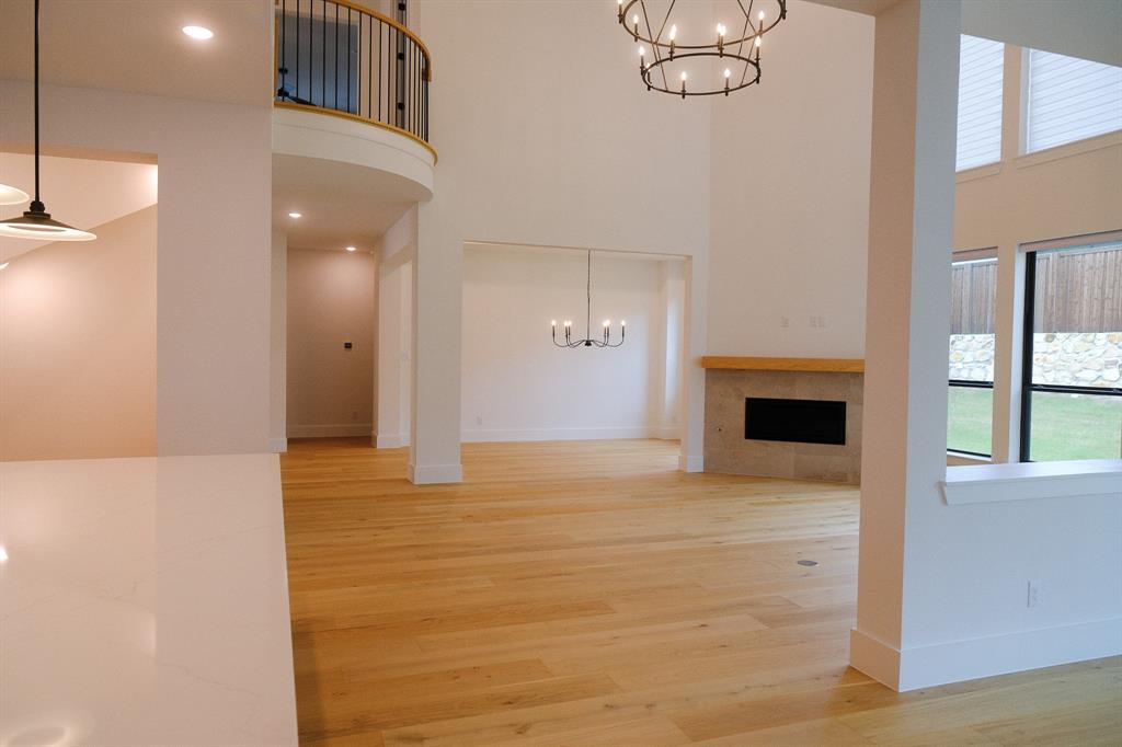 Two-story ceiling height, light-toned wood-finish flooring, fireplace with stone surround and wood mantel, iron chandelier lighting, and a curved balcony with iron railing