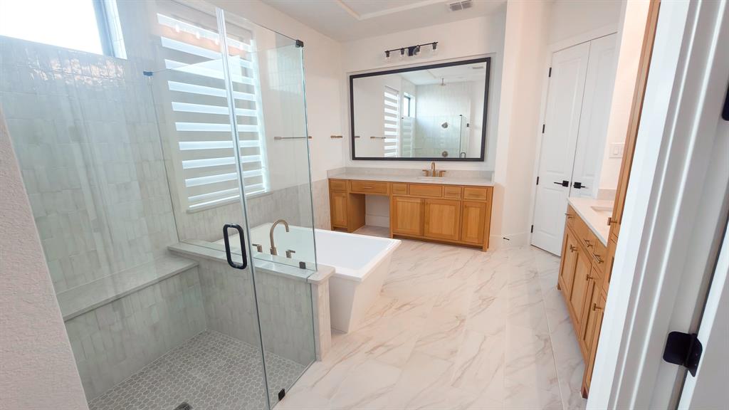 Bathroom featuring a glass-enclosed walk-in shower with tile surround, a freestanding soaking tub, dual wood-finish vanities, and oversized mirrors