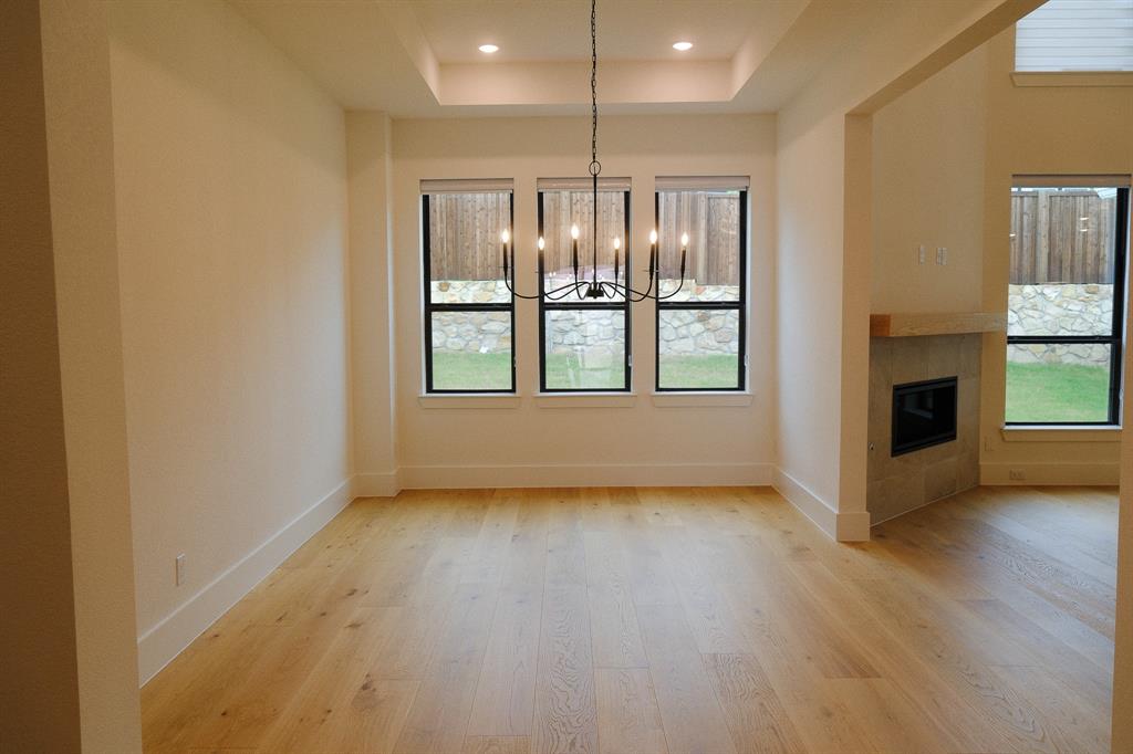 Dining area featuring wood-finish flooring, a tray ceiling with recessed lighting, a multi-arm chandelier, and a fireplace with a stone surround and timber mantel