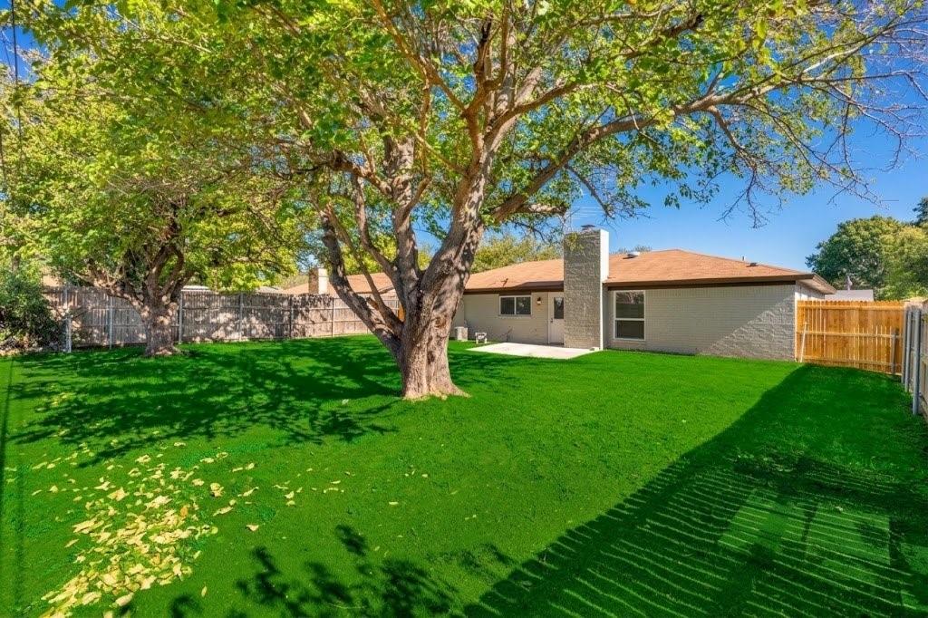 Backyard featuring mature trees, concrete patio, masonry chimney, and perimeter wood fencing