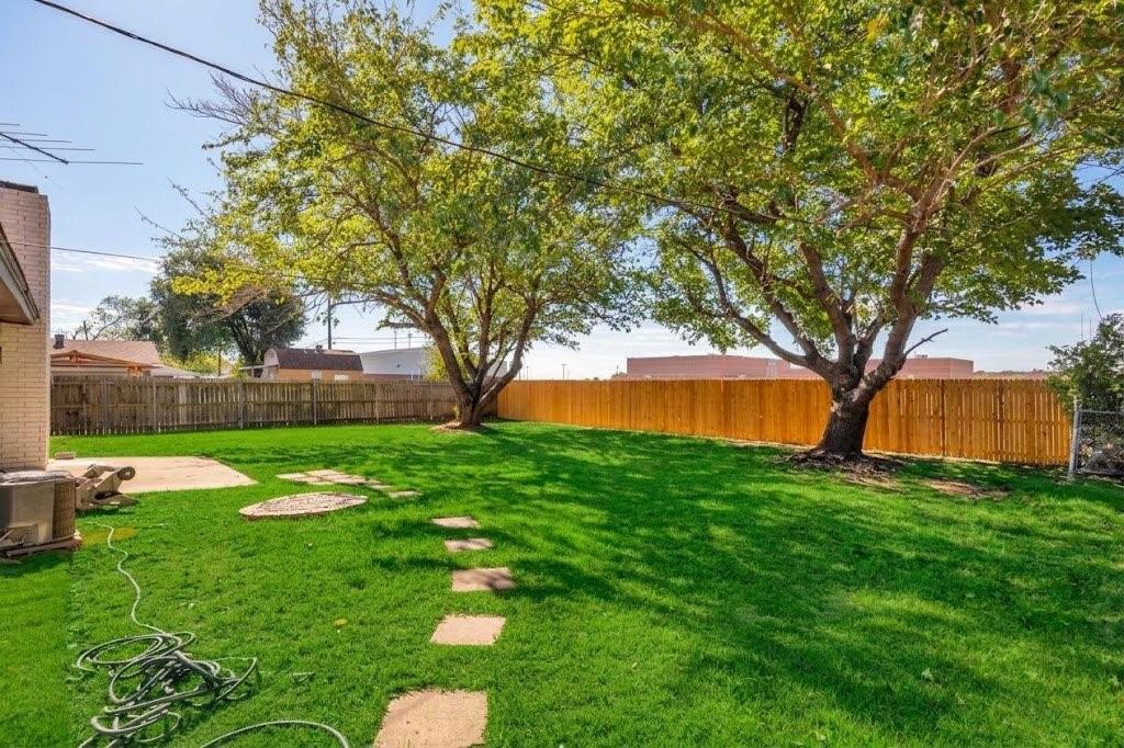 Expansive backyard featuring a level lawn, mature trees, wood privacy fencing, and concrete hardscaping