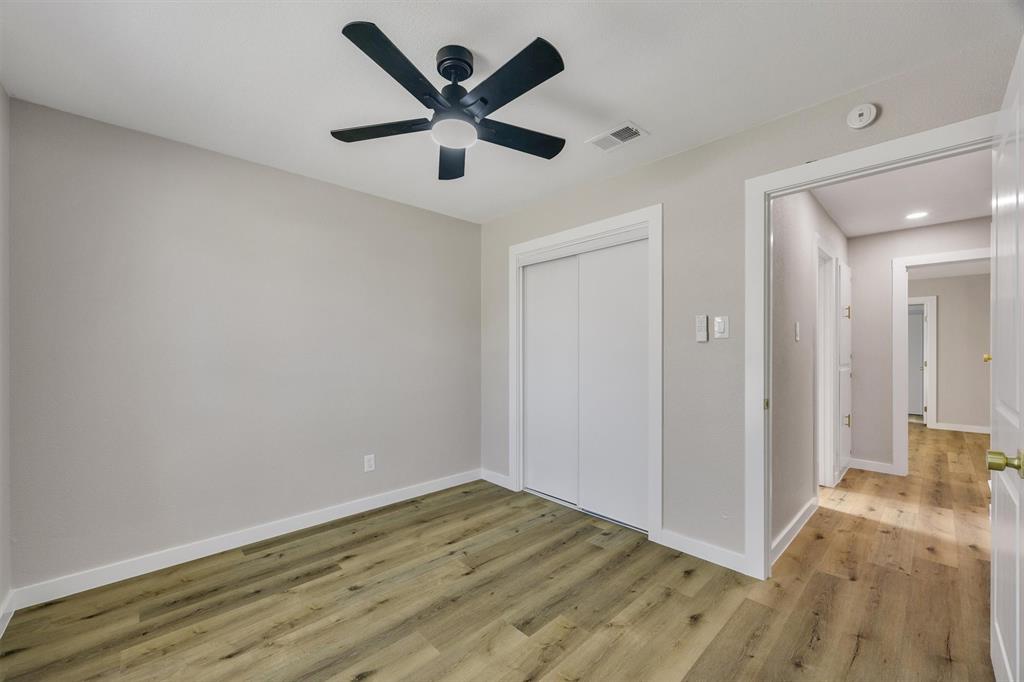 Room featuring wood-finish flooring, a five-blade ceiling fan with integrated lighting, and a closet with sliding doors