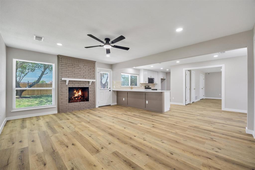 Open-concept space featuring wood-finish flooring, a floor-to-ceiling brick fireplace with a wood mantel, a center kitchen island with bar seating, and recessed lighting