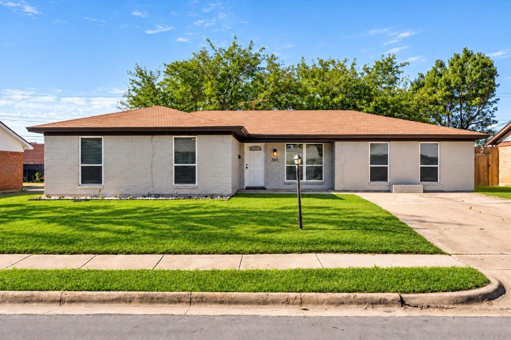 Single-story brick exterior featuring a hipped roof, multi-pane windows, a paved driveway, and a level lawn