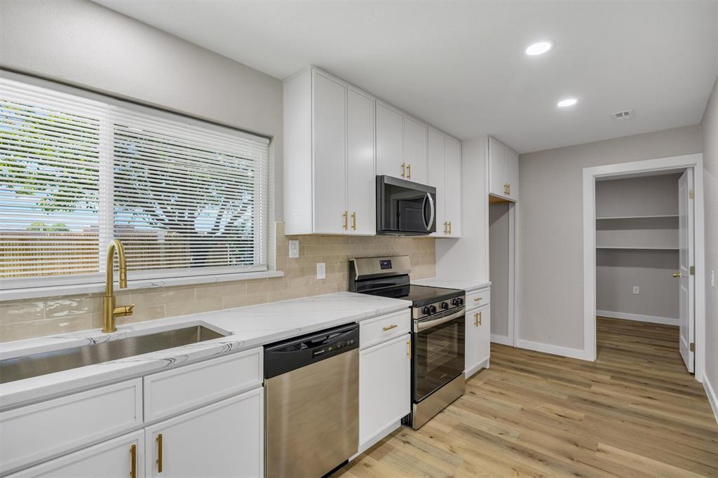 Kitchen featuring white shaker cabinetry, gold-tone hardware, light stone countertops, stainless steel appliances, and wood-finish flooring