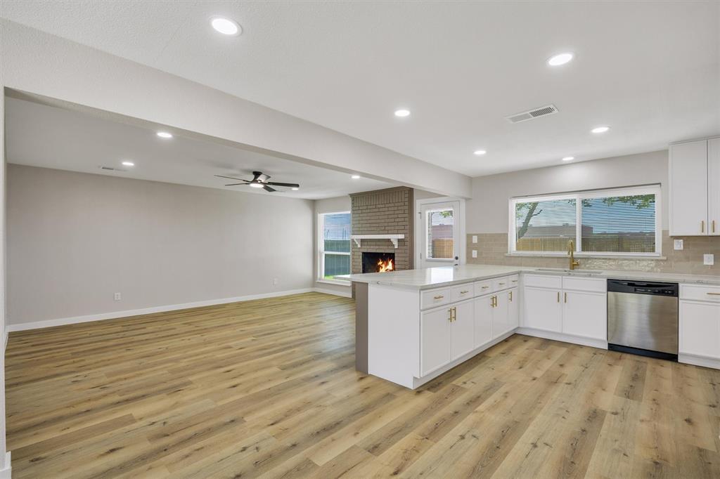 Open-concept living space featuring wood-finish flooring, recessed lighting, a brick fireplace, white cabinetry, and a kitchen island with stone-surface countertops