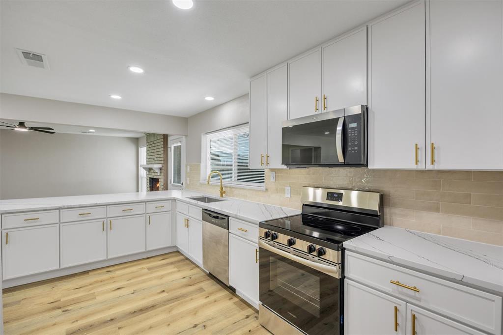 Kitchen featuring white cabinetry with gold-tone hardware, stone-finish countertops, stainless steel appliances, a tile backsplash, and wood-finish flooring