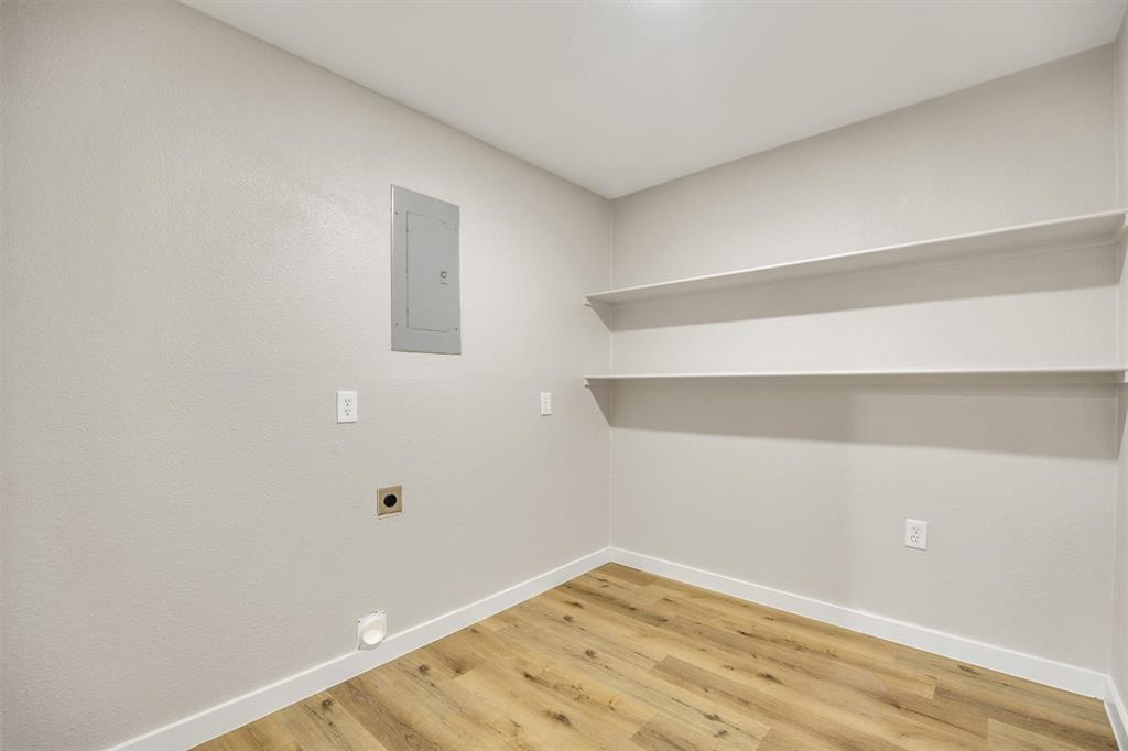 Utility area featuring wood-finish flooring, two levels of fixed wall-mounted shelving, and a recessed electrical service panel