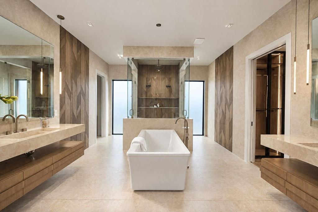 Soak away stress in the freestanding tub framed by seamless porcelain slab walls, dimensional tile, and warm wood vanities