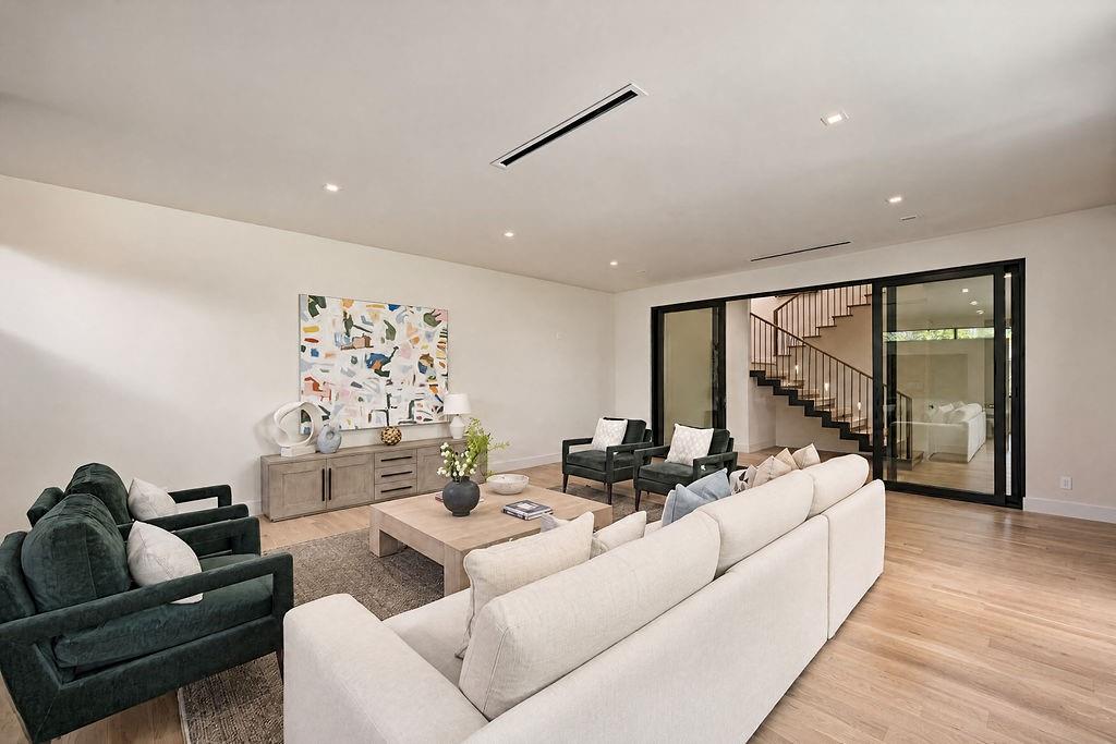 Lounging here feels grounded and effortless, framed by soft architectural ceiling lights and the dramatic backdrop of the floating wood stairs