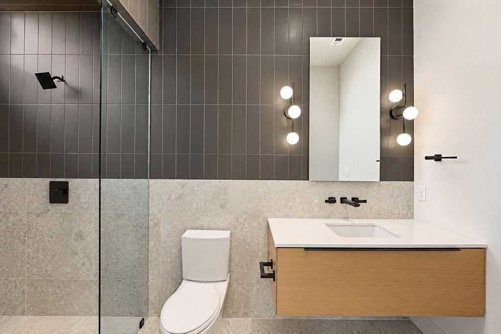 Enjoy a private guest experience complete with a float-mounted wood vanity, modern wall sconces, and a dark tiled shower surround