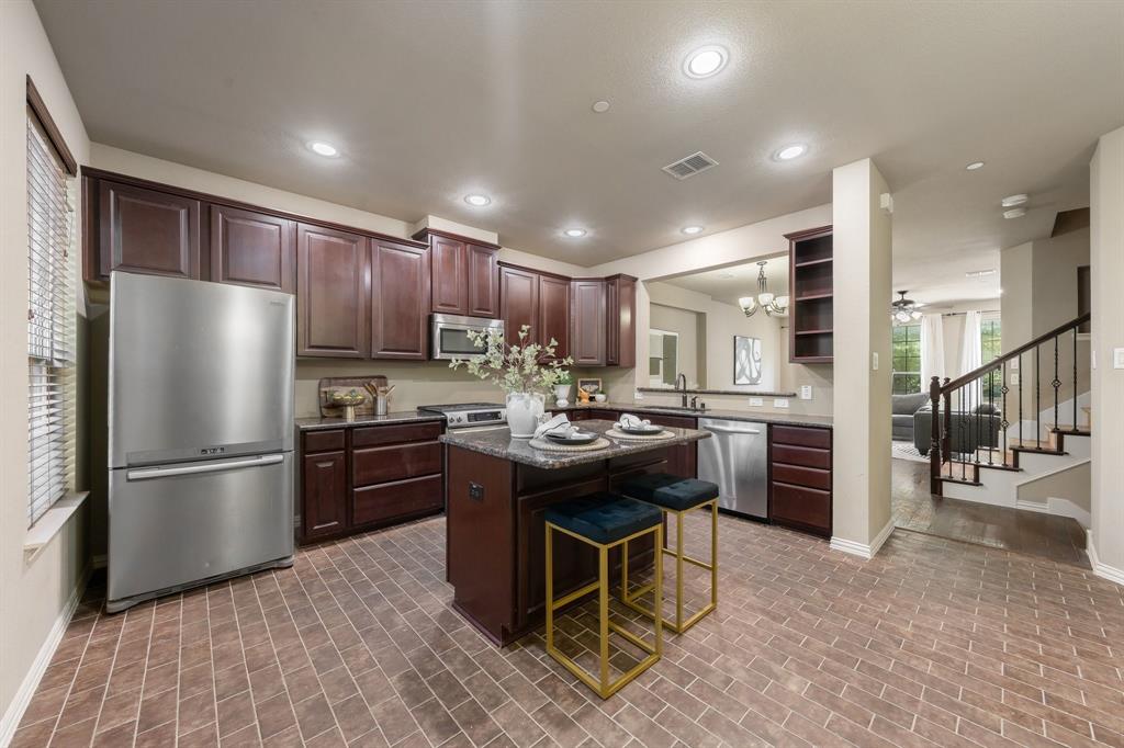 Kitchen featuring dark wood cabinetry, a central island with stone-finish countertop, stainless steel appliances, and tile flooring