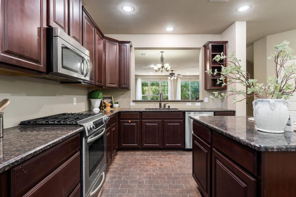 Kitchen featuring dark wood cabinetry, stone countertops, stainless steel appliances, brick-style tile flooring, and recessed lighting