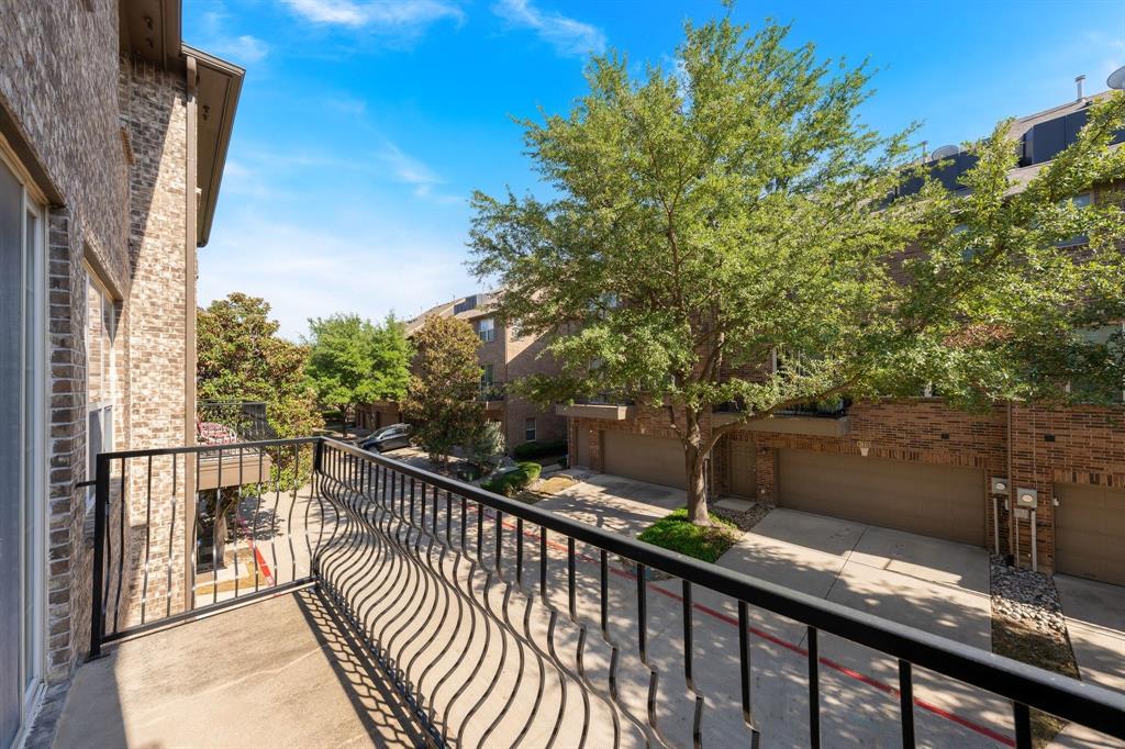 Private balcony featuring a black metal railing and concrete flooring overlooking brick exterior masonry and mature landscaping