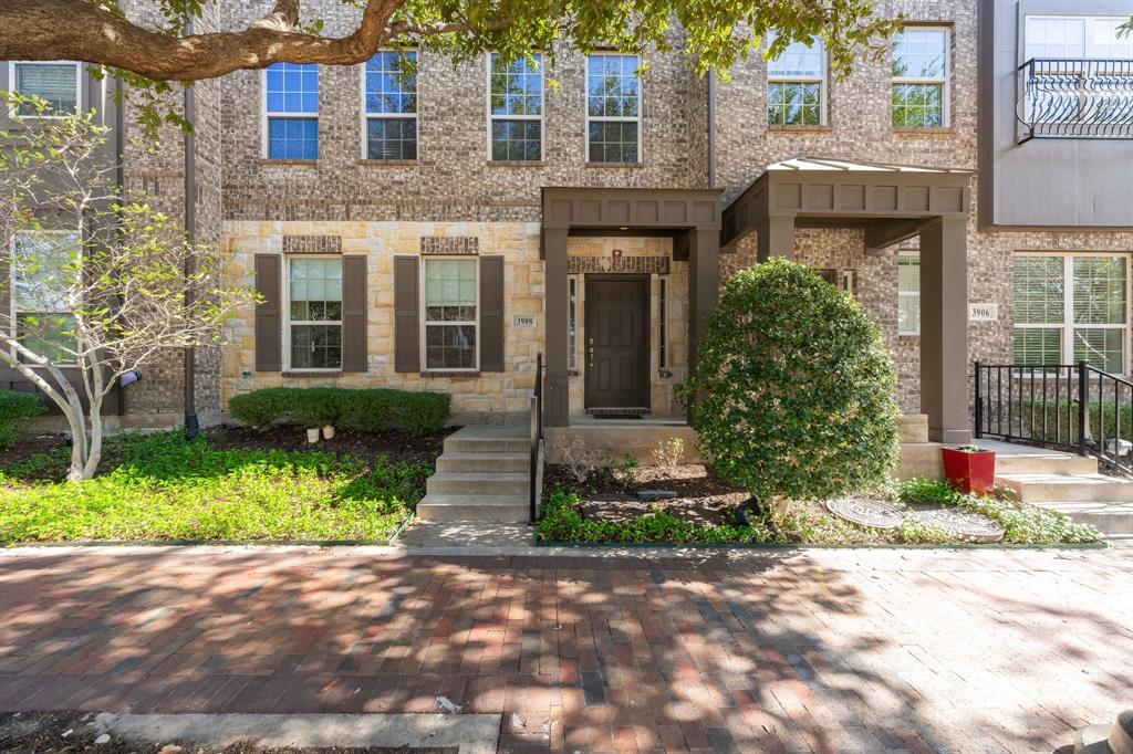 Multi-story brick exterior featuring light-toned stone accents, decorative brown shutters, covered entryway, and a brick-paved driveway
