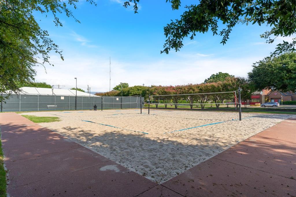 Sand volleyball court featuring a permanent net, perimeter fencing, and concrete borders