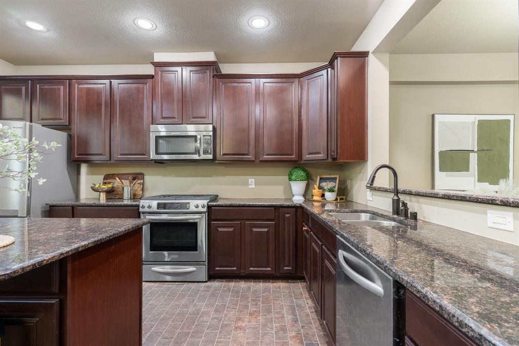 Kitchen featuring dark wood-finish cabinetry, stone-finish countertops, stainless steel appliances, a double-basin sink with a high-arch faucet, and tile flooring