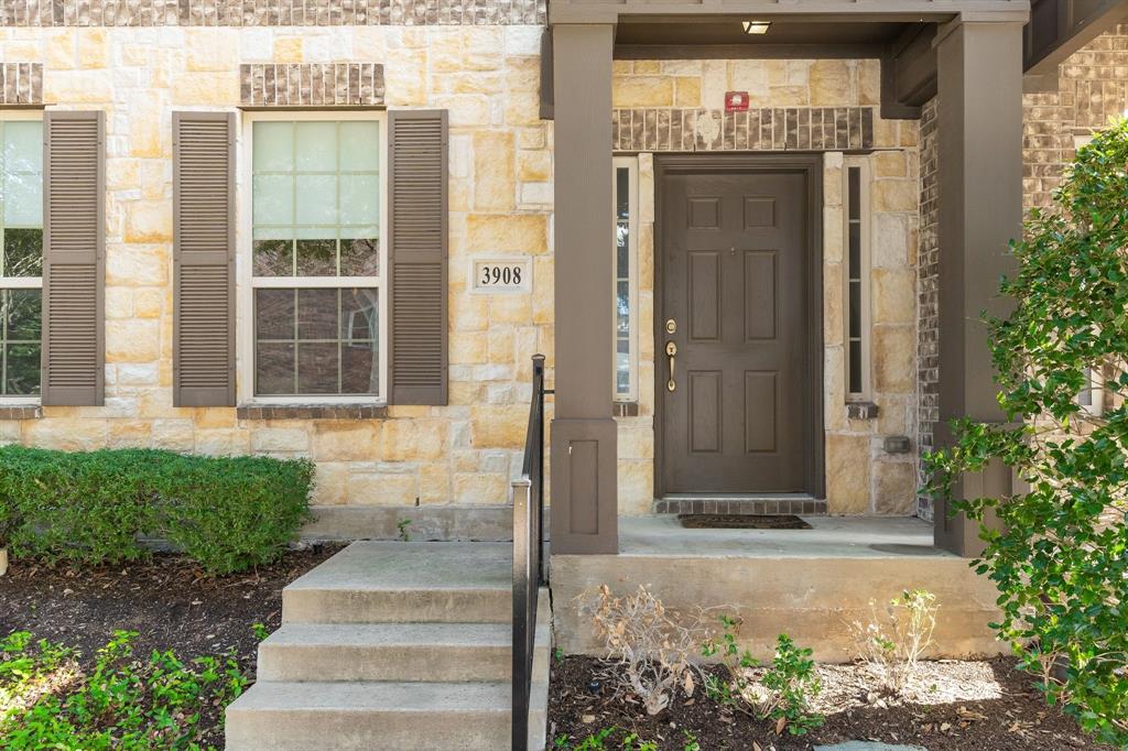 Stone veneer exterior with dark-toned shutters, covered entryway, concrete steps with metal railing, and multi-pane windows