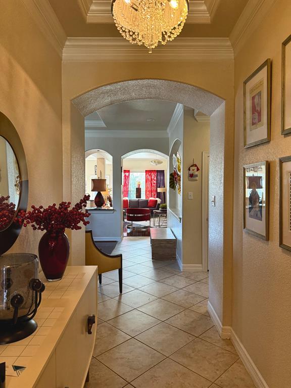Foyer featuring a recessed tray ceiling, crystal chandelier, arched architectural entryways, and tile flooring
