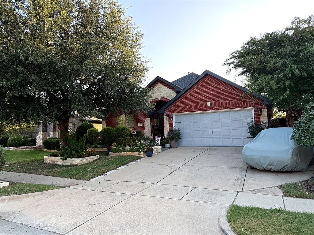 Traditional exterior featuring red brick and stone masonry, multi-gabled roofline, concrete driveway, and established landscape with mature trees and stone-bordered garden beds