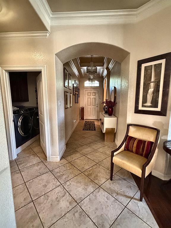 Foyer featuring ceramic tile flooring, arched architectural detailing, crown molding, and recessed tray ceiling with a central chandelier