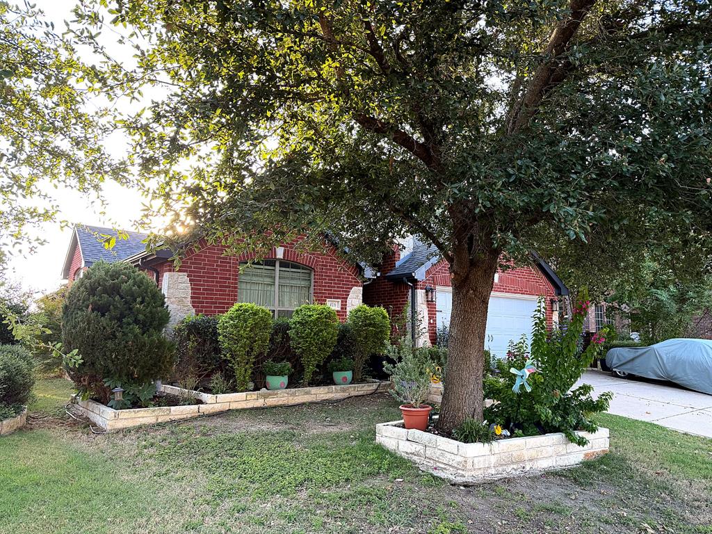 Red brick exterior featuring limestone masonry accents, arched window detailing, a multi-car garage, and tiered stone garden beds