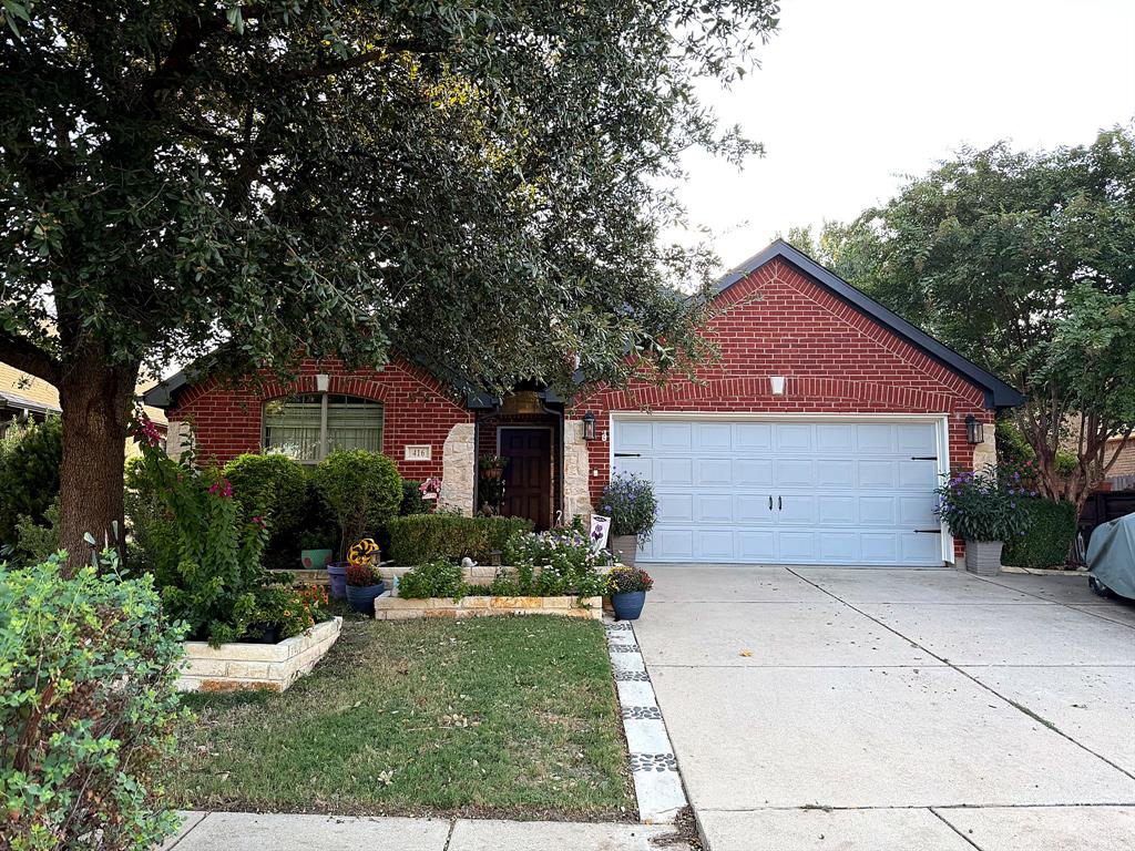 Traditional brick exterior featuring stone masonry accents, an attached two-car garage, and tiered stone landscaping beds