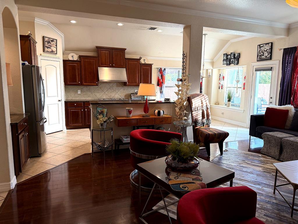 Kitchen featuring dark wood cabinetry, stainless steel range hood, stone-surface countertops, and tile backsplash, complemented by wood-finish flooring and recessed lighting